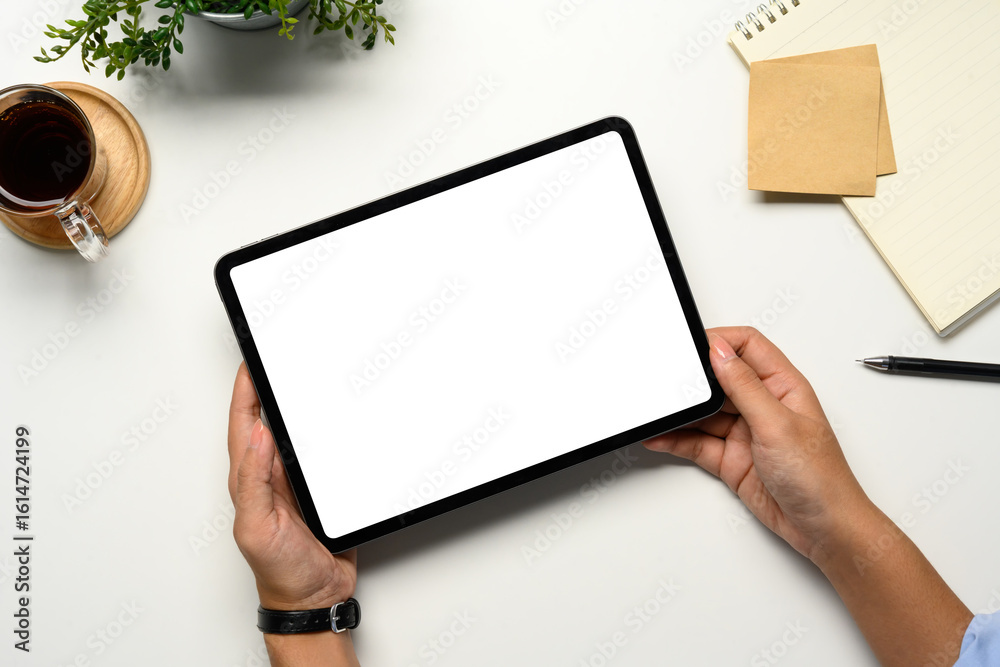Obraz premium Hands holding a digital tablet with a blank white screen on a clean desk