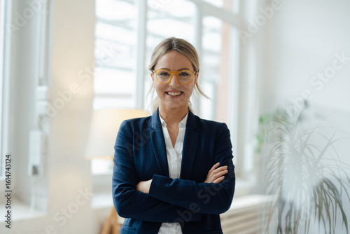 Happy businesswoman standing with arms crossed in office