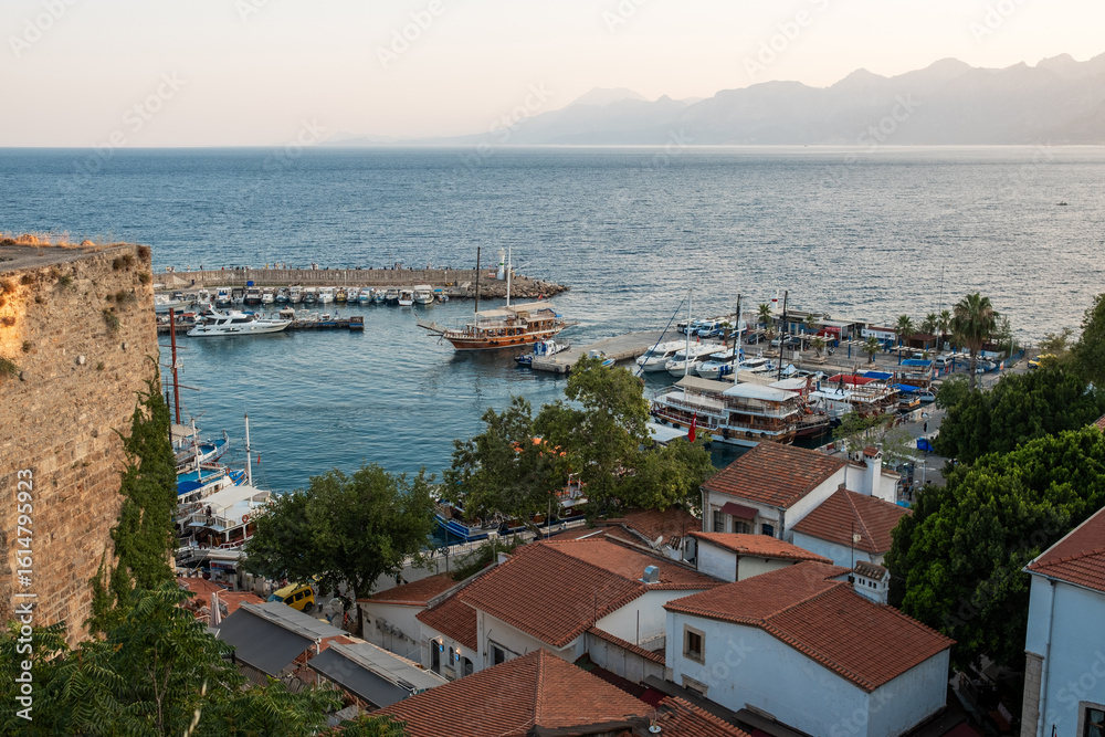 Obraz premium Coastal View of a Bustling Marina With Boats and Charming Rooftops in the Golden Hour Light of a Serene Seaside Town
