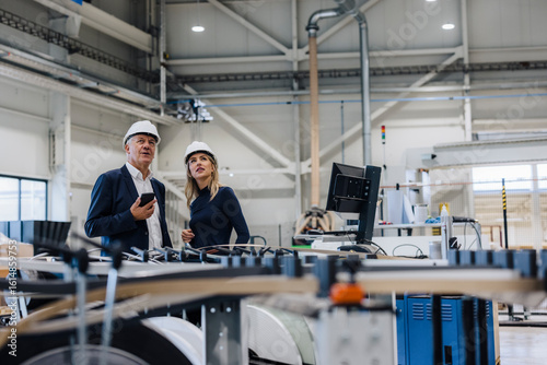 Businessman and colleague standing near machine in factory