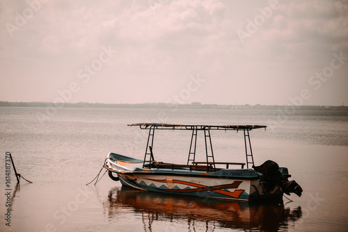 A traditional fishing boat rests calmly on shallow waters under a cloudy sky. With vibrant colors and a simple frame, it captures the peaceful charm of coastal life and maritime tradition.
