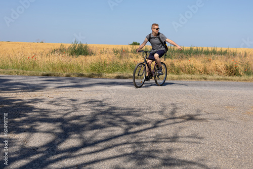 Valokuva A man riding a bicycle gestures with his hand to indicate a direction while traveling along a rural road