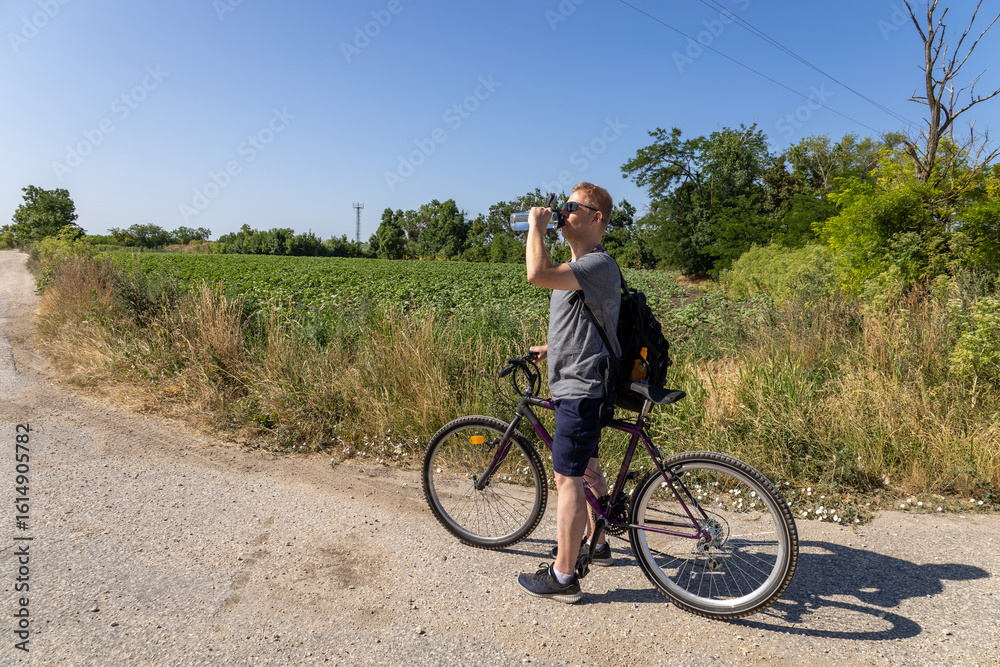 Obraz premium Cyclist drinking water on a rural summer road 