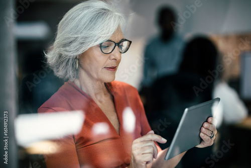 Senior businesswoman using tablet PC seen through glass window
