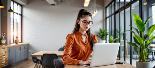 Focused young woman working on laptop in modern office professional environment indoor workspace creative concept