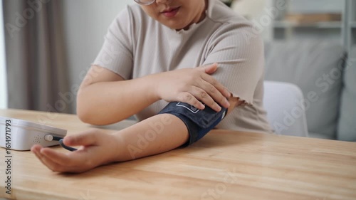 An Asian woman uses a portable blood pressure monitor in her living room. Health awareness concept.