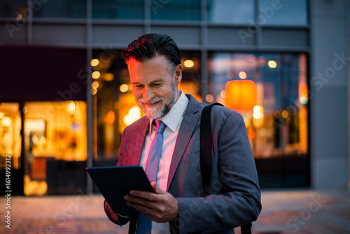 Smiling mature businessman using tablet PC on footpath