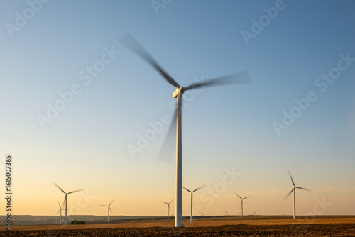 Renewable wind farm in rural region, turbines spinning under clear sky, producing clean energy without emissions, supporting environmental sustainability goals, future of energy captured in scenic