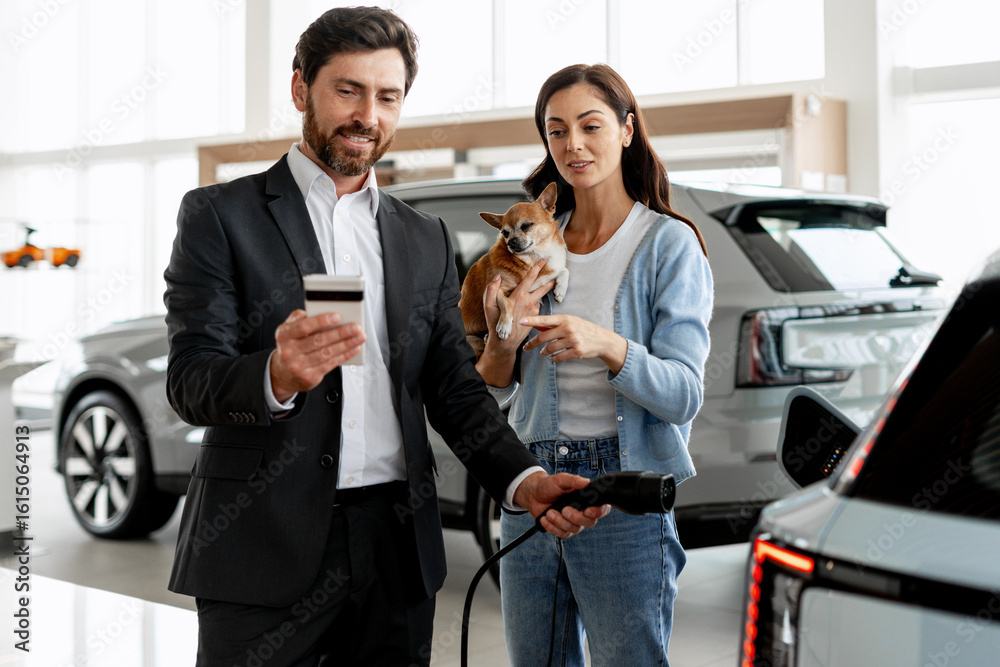 Obraz premium Car salesman showing credit card and charging station to woman holding chihuahua