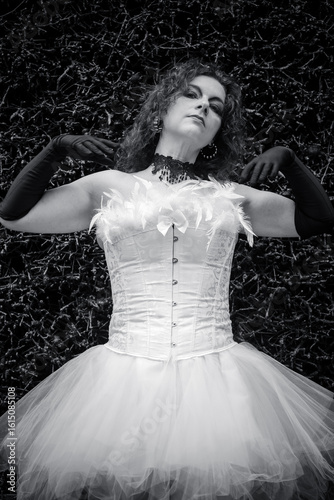 Elegant dancer in a dramatic pose wearing a white costume adorned with feathers against a dark textured backdrop