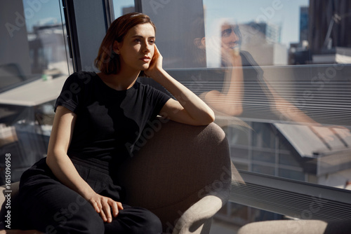 Thoughtful young businesswoman sitting on chair near window at office
