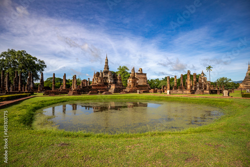 View of Wat Mahathat temple reflected in a pond and blue sky in Sukhothai Historical Park, Thailand