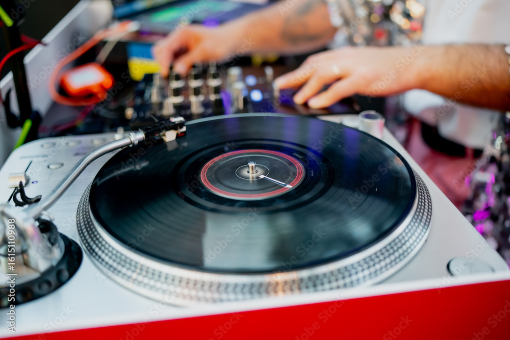 Obraz premium DJ turntable and vinyl record player with mixing console, hands adjusting audio controls during live performance, professional DJ equipment for music mixing and entertainment
