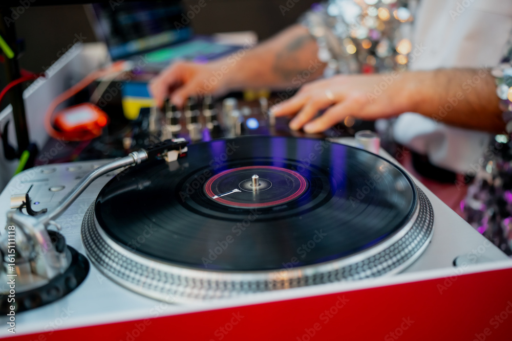 Obraz premium Vinyl turntable and DJ hands adjusting mixer controls during music event, professional DJ setup with record spinning, mixing board and audio equipment for live performance