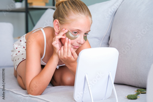 The girl looks in the mirror. The teenager put gel  patches under her eyes.
