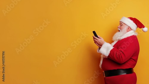 Santa in bright red suit checking his phone against cheerful yellow backdrop