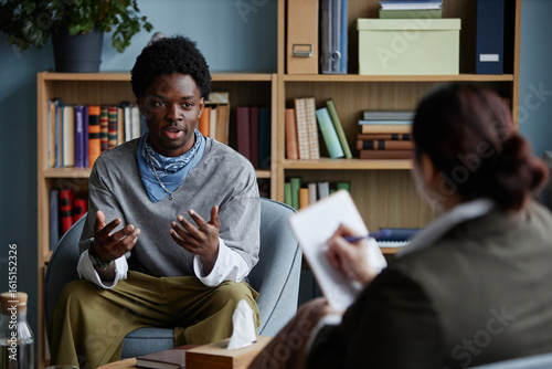 Φωτογραφία Black teenage boy sitting and talking with adult woman counselor during counseli