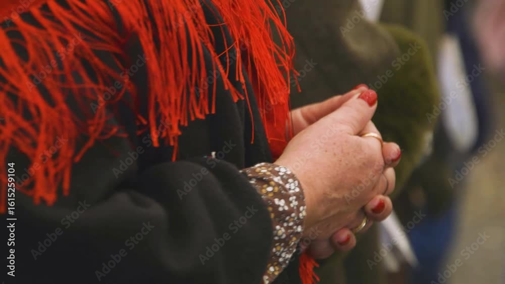 Woman with red nails clasping hands, red shawl, bracelets. Detail shot.