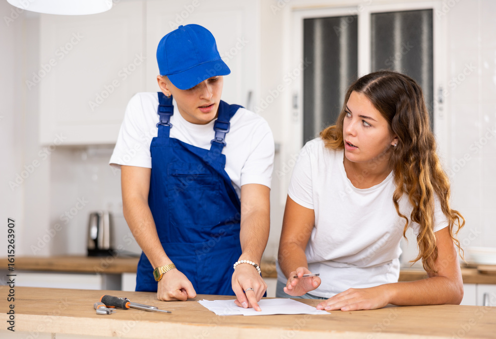 Obraz premium Positive professional plumber tells an young housewife where to sign an invoice for work performed.