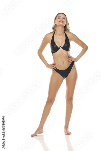 Studio shot of blonde woman in black bikini smiling and posing confidently on white background.