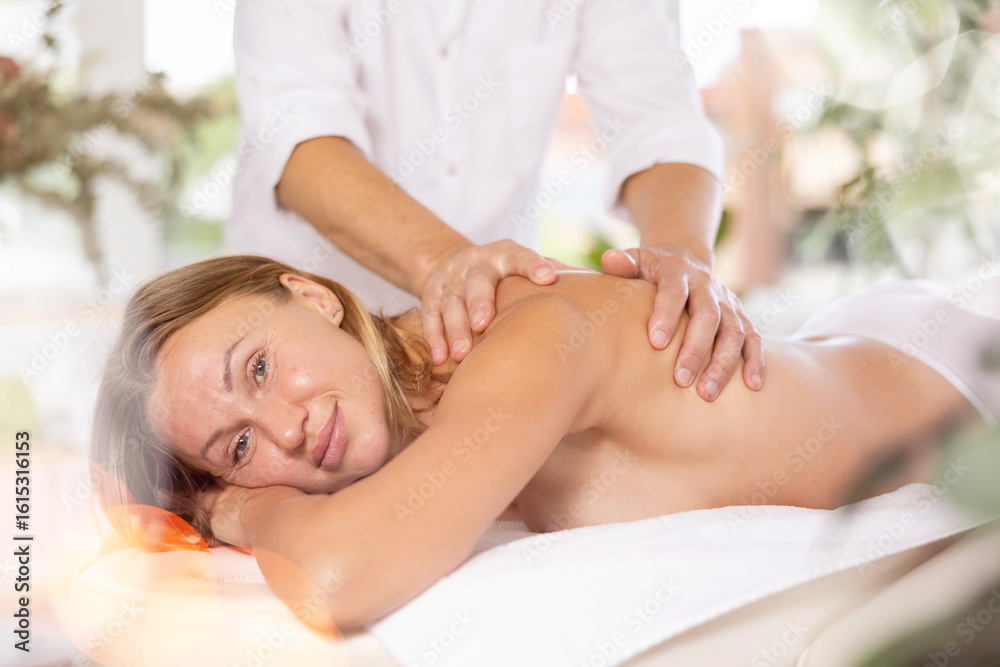 Obraz premium Relaxed middle-aged woman undergoing back massage therapy conducted by skilled masseur in light room