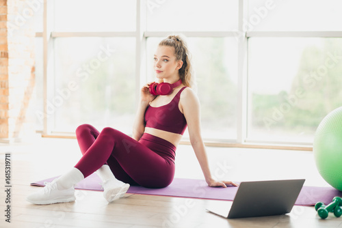 Young sportswoman in activewear relaxing with headphones, sitting on home yoga mat during a workout break