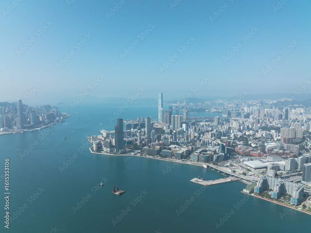 Fototapeta premium Jan 11, 2022 - Hong Kong, China: Aerial view of Hong Kong cityscape with Victoria Harbor, waterfront, urban buildings, and ocean under clear sky.