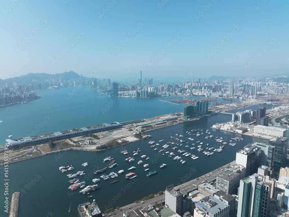 Obraz premium Breathtaking aerial view of central Hong Kong, China, displaying the vast cityscape, harbor with boats, and distant mountains under a clear sky.