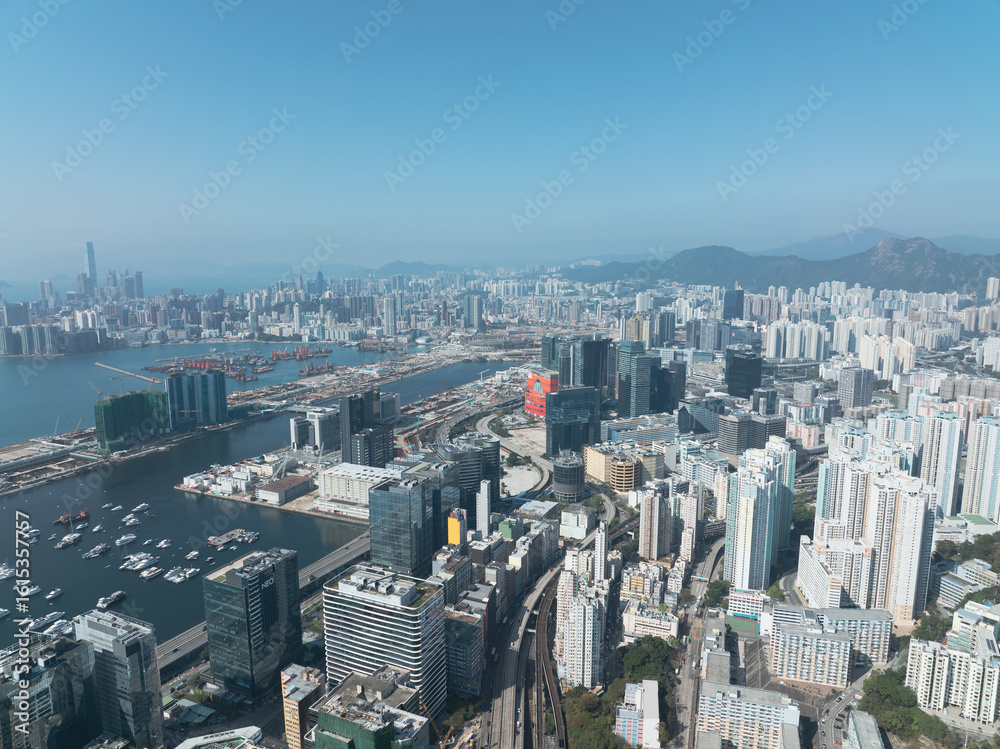 Fototapeta premium Aerial view of central Hong Kong, China, showcasing a dense cityscape. Buildings sprawl towards the harbor under a clear blue sky, with distant mountains.