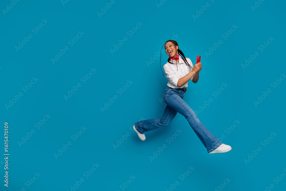 Fototapeta premium Young stylish woman jumping joyfully while holding a smartphone, showcasing vibrant personality and casual fashion