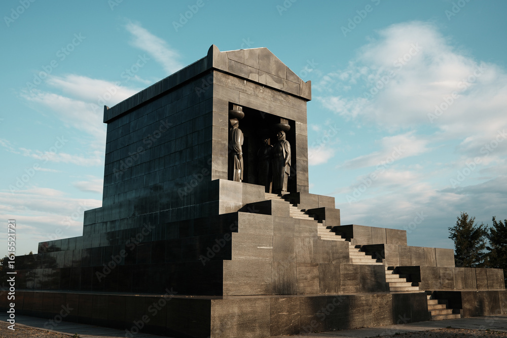 Fototapeta premium Side angle of the Monument to the Unknown Hero in Belgrade, Serbia. Solid granite structure with statues under a bright blue sky at sunset.