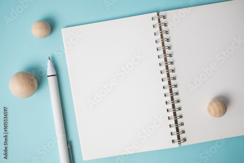 Workspace with empty notebook, pen and wooden ball on blue background.
