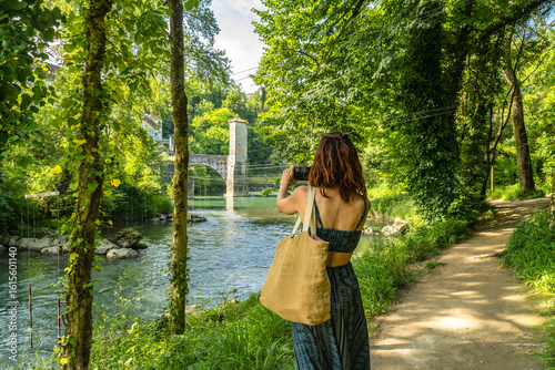 Obraz na plátně Tourist taking pictures of the gave d'oloron river and old bridge in sauveterre