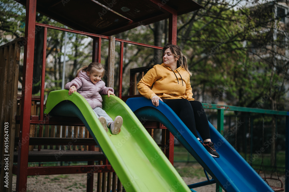 Fototapeta premium A mother and her young daughter spend quality time together at a park playground, using slides.