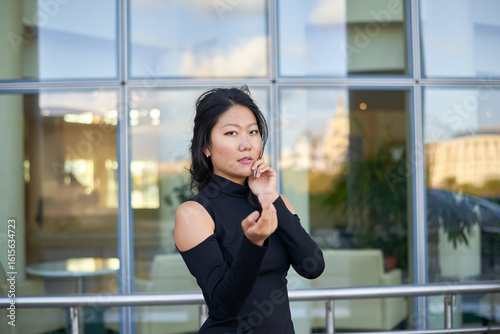 Free Download A lady in a black outfit is standing outside the house. She's wearing elegant stilettos. The tight-fitting dress highlights her graceful curves. - GFXLoad