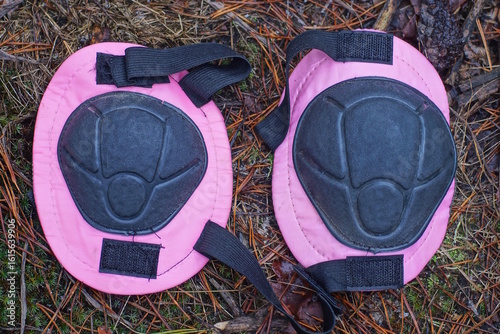 two of colored pink black plastic knee pads lie on brown ground and green moss in white snow on winter street