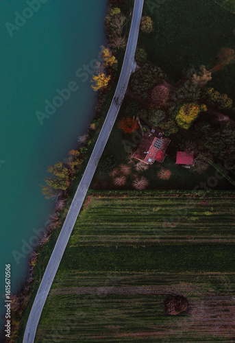 Aerial view of the tranquil lake waters contrasting with the vibrant autumn foliage and red-roofed houses along the shore, Milan, Lombardy, Italy.