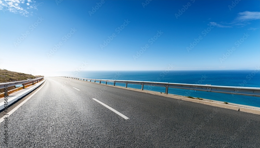 Fototapeta premium asphalt road leading to ocean with clear blue sky great for vacation banners or transportation concepts