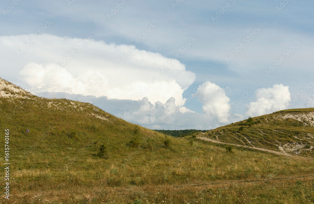 Fototapeta premium A scenic landscape featuring rolling hills and a clear blue sky with fluffy white clouds