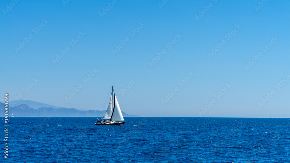 Fototapeta premium White-sailed sailing yacht sails across Mediterranean or Aegean Sea against background of islands. Boat trips, yachting. Free lifestyle