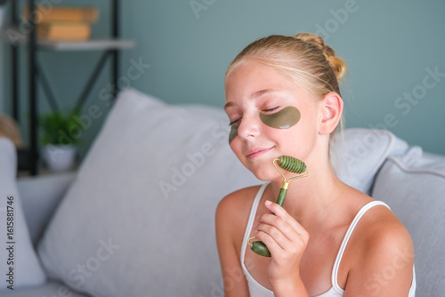 A girl is doing a facial massage with a massager. The teenager put gel patches under her eyes.