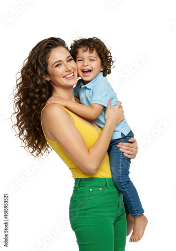 A joyful young caucasian woman with voluminous curly hair in yellow top & green pants tenderly embraces a laughing little boy in blue polo against a transparent studio background with copy space.