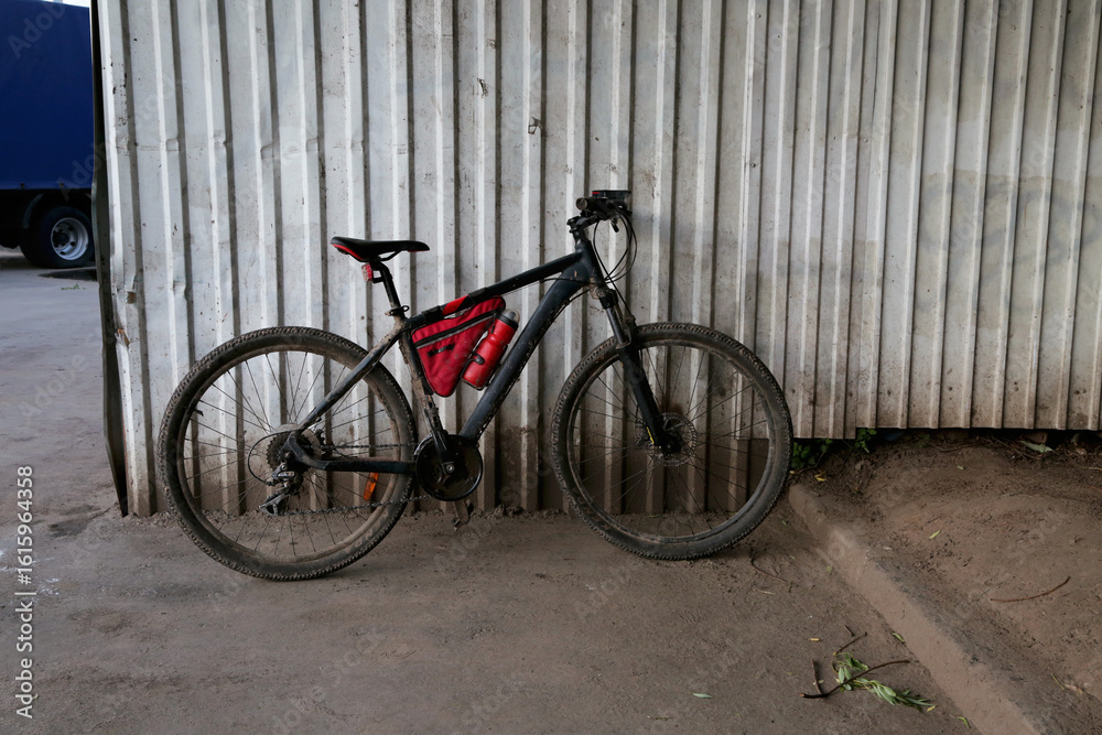 Black spot bike on the city street standing on the road near the grey wall garage building Black spot bike on the city street standing on the road near the grey wall garage building