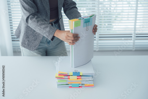 Fotografie Stack of Organized Papers: A person carefully organizes a stack of documents with colored tabs, showcasing attention to detail and the value of structured information