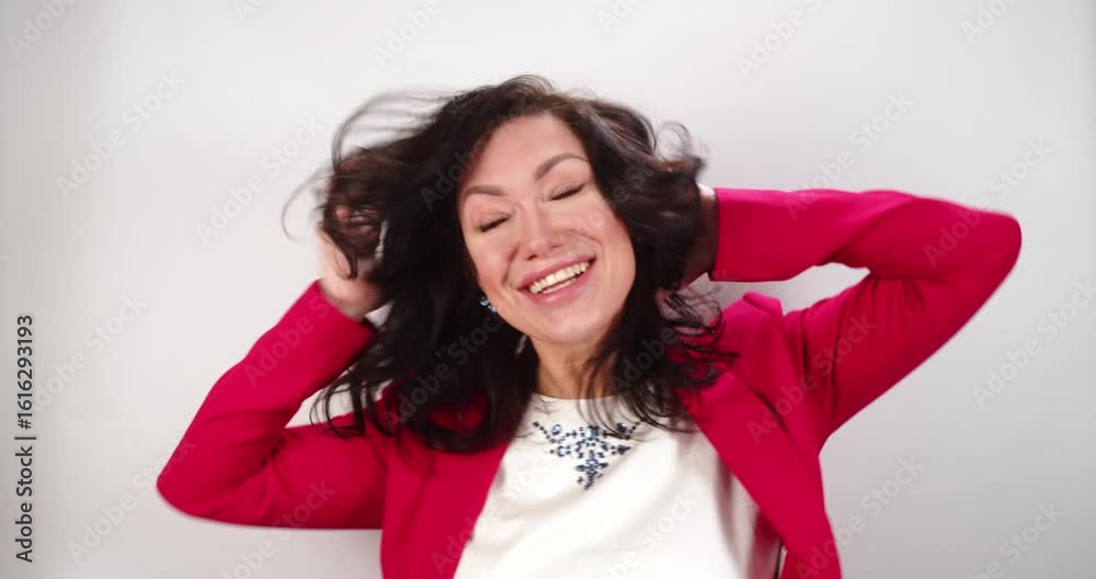Woman playfully interacts with camera, smiling and joking with lively gestures, dressed in red blazer against grey wall Woman playfully interacts with camera, smiling and joking with lively gestures, dressed in red blazer against grey wall