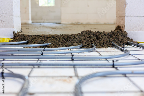 Underfloor heating installation with fresh screed,Construction site showing underfloor heating pipes being covered with fresh cement screed during flooring installation in a building.
