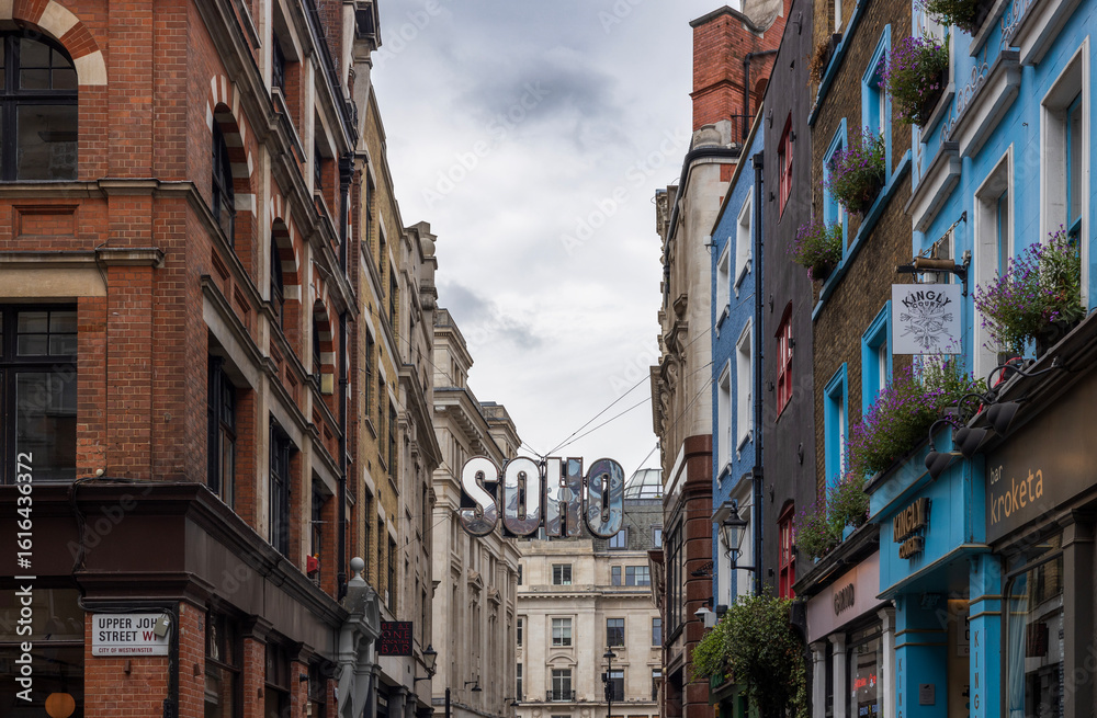 Obraz premium A view down a street of Soho in London with a big silver Soho sign suspended above it.