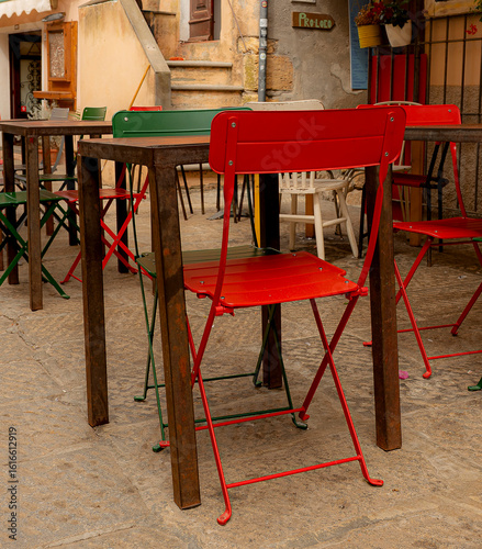 Colorful iron chairs and wooden tables with stairs and vases in the background