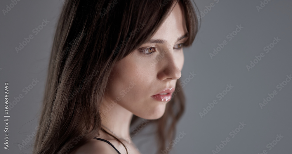 Beautiful woman with long brown hair looking down on gray background Beautiful woman with long brown hair looking down on gray background