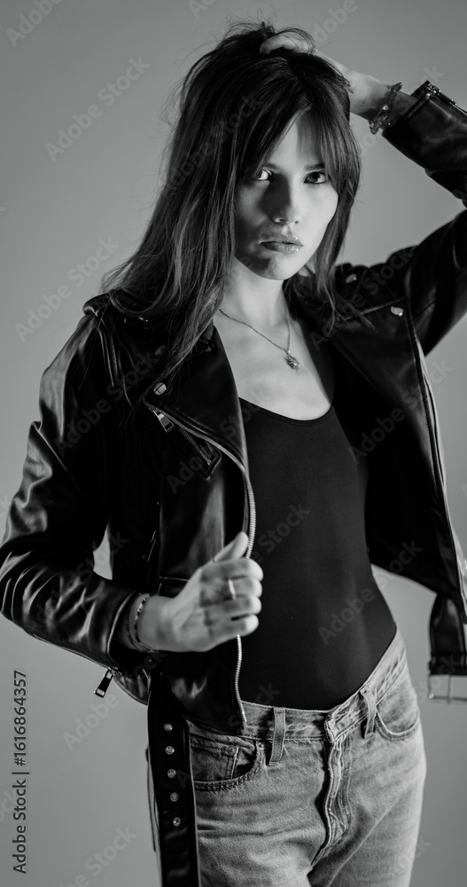 Fototapeta premium Fashionable young woman with long hair wearing leather jacket and jeans posing in studio